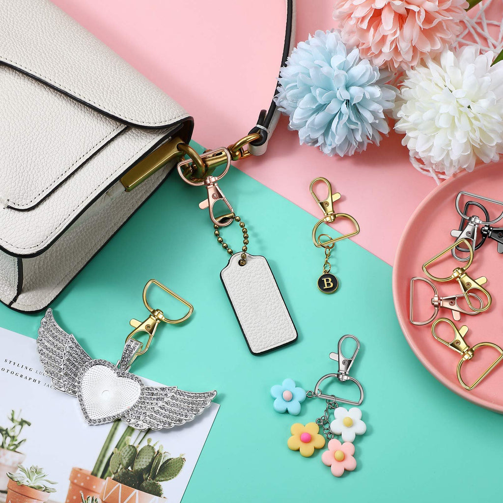 Keychain making kit components including swivel clasps, D-rings, a heart-shaped charm with wings, a blank tag, and flower charms, arranged around a white handbag.