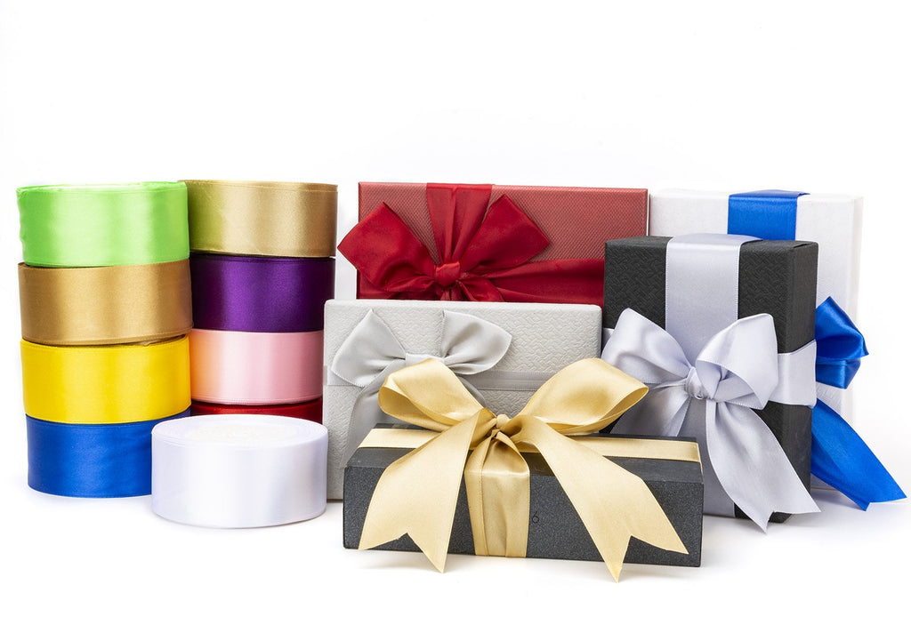 Assortment of colorful satin ribbon rolls and gift boxes with bows on a white background.
