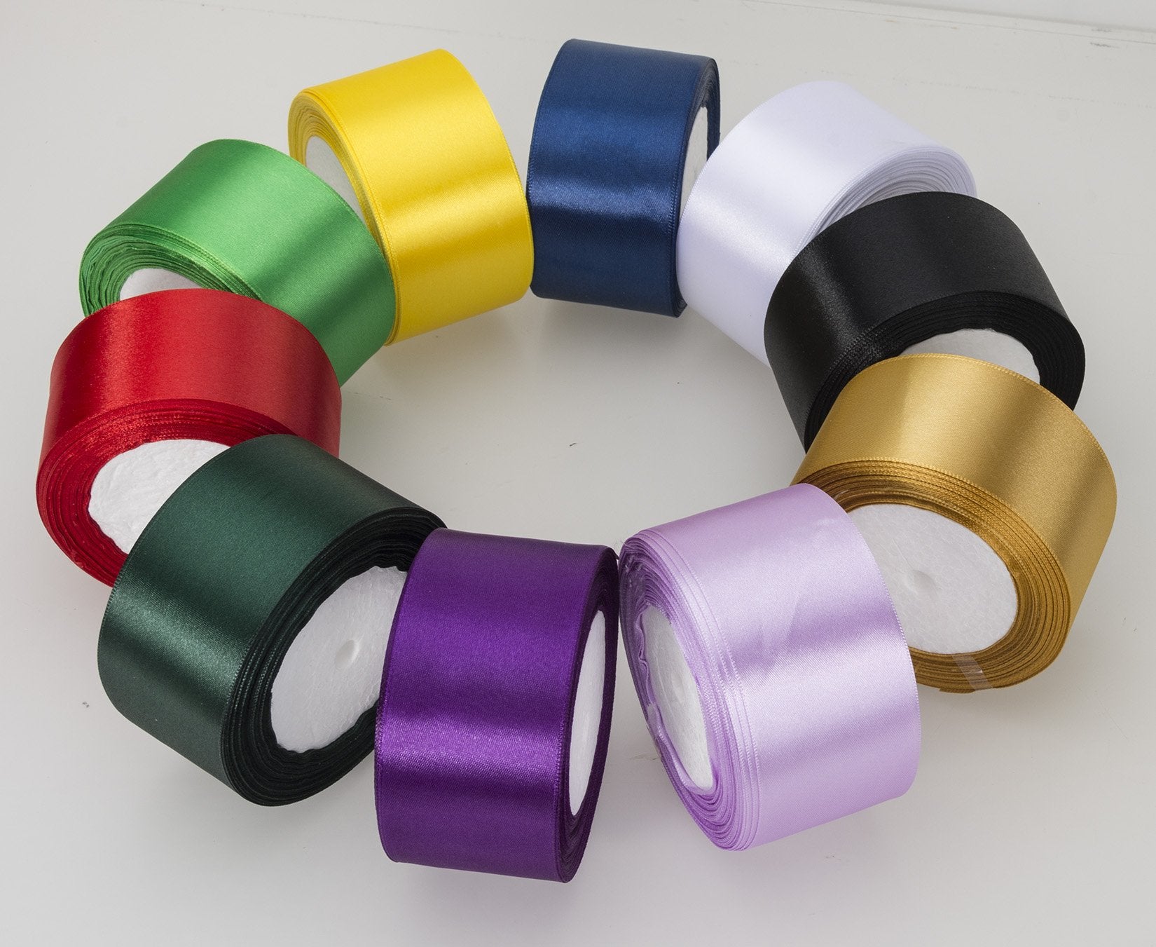 Collection of satin ribbon rolls in various colors arranged in a circle on a white surface.