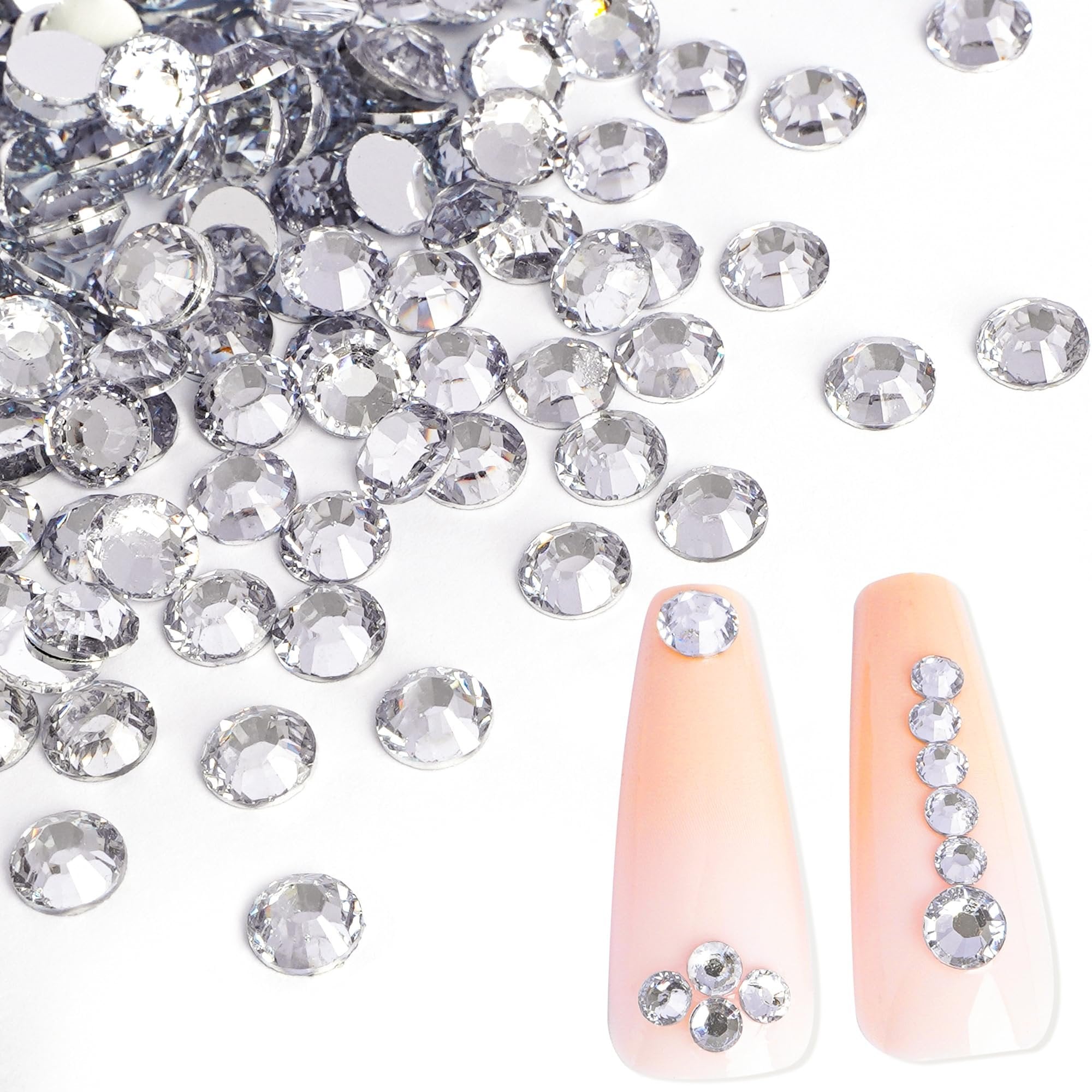 Clear flatback rhinestones scattered on a white surface with two nail tips decorated with rhinestones.