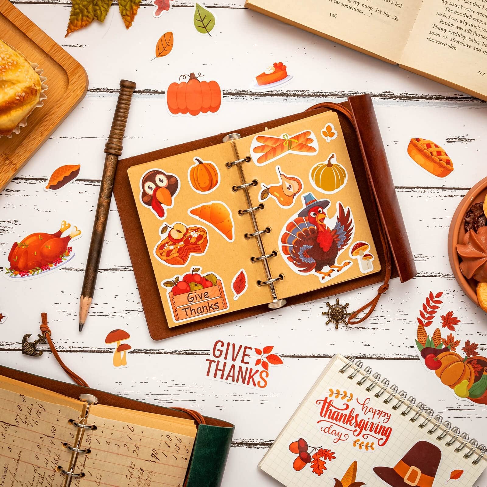 Autumn stickers including pumpkins, turkeys, pies, and leaves scattered around an open notebook and a book.