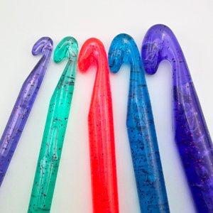 Five large plastic crochet hooks in purple, green, red, blue, and dark purple, with glitter flecks, arranged in a row against a white background.