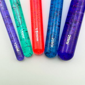 Close-up of five large plastic crochet hooks with glitter, showing size markings 12mm, 15mm, 18mm, 20mm, and 25mm.