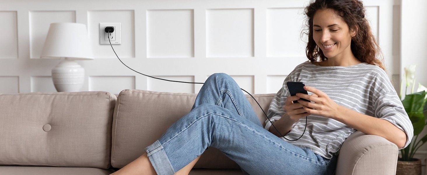 Woman sitting on a couch, charging her phone with a USB C wall charger plugged into an outlet.