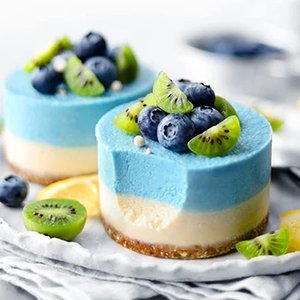 Two layered cheesecakes topped with blueberries, kiwi slices, and lemon on a white platter.