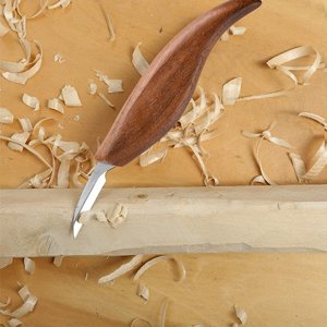 Wood carving knife with wooden handle cutting into a wooden block, surrounded by wood shavings