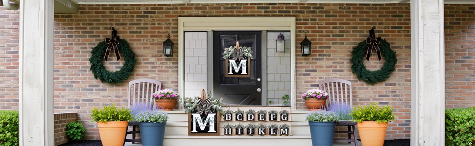 Front porch decorated with two wreaths, potted plants, chairs, and alphabet letter signs.