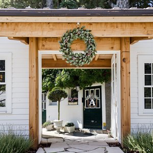 Eucalyptus garland wreath with pink berries and a bow hanging on a wooden archway above a doorway.