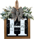 Front door wreath with eucalyptus garland, white flowers, and a black and white striped bow, featuring large white letters and 'Welcome to Our Home' text.