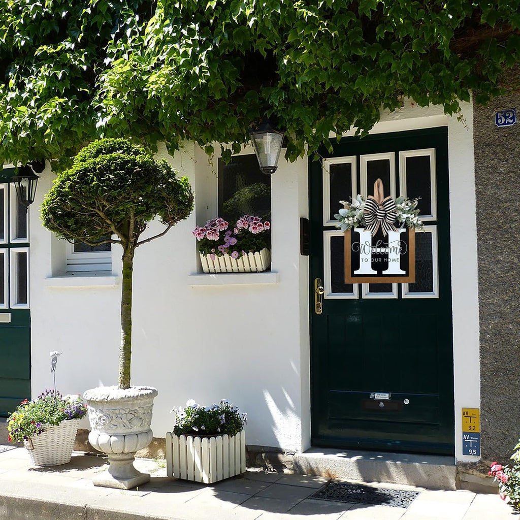 Front door decorated with a wreath featuring eucalyptus, a bow, and a wooden monogram sign with 'Welcome To Our Home' text.