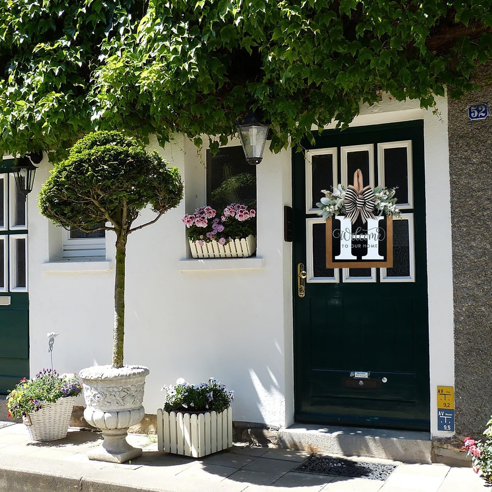 Front door decorated with a wreath featuring eucalyptus, a bow, and a wooden monogram sign with 'Welcome To Our Home' text.