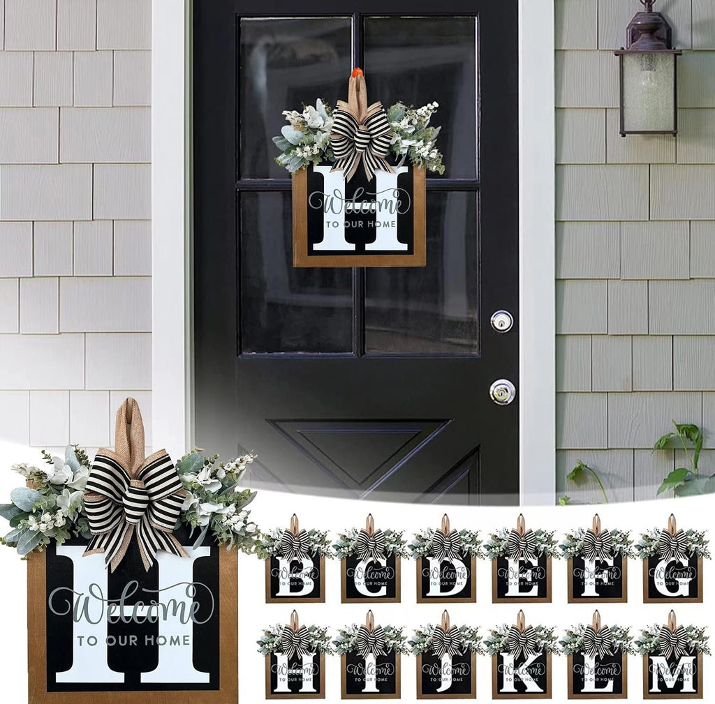 Front door wreath with eucalyptus garland, bow, and wooden monogram sign displaying the letter H and 'Welcome to Our Home'.
