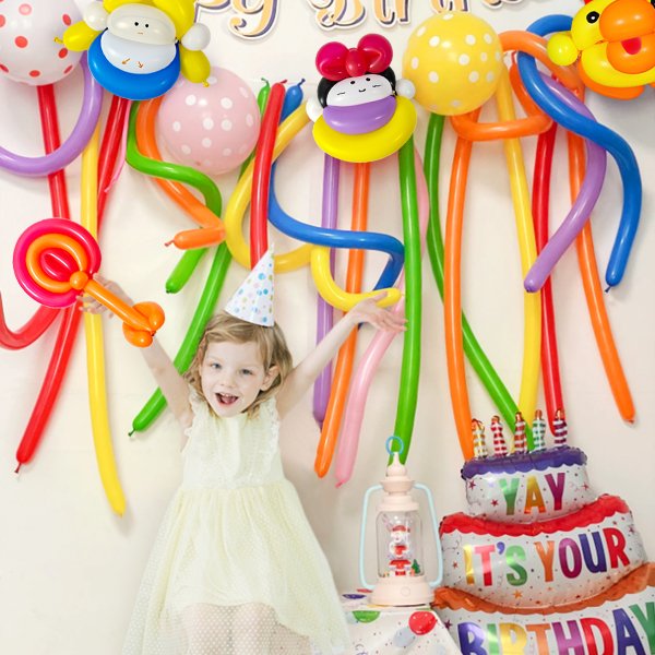 Young girl in a party hat with arms outstretched, surrounded by colorful twisting balloons and a birthday cake balloon.