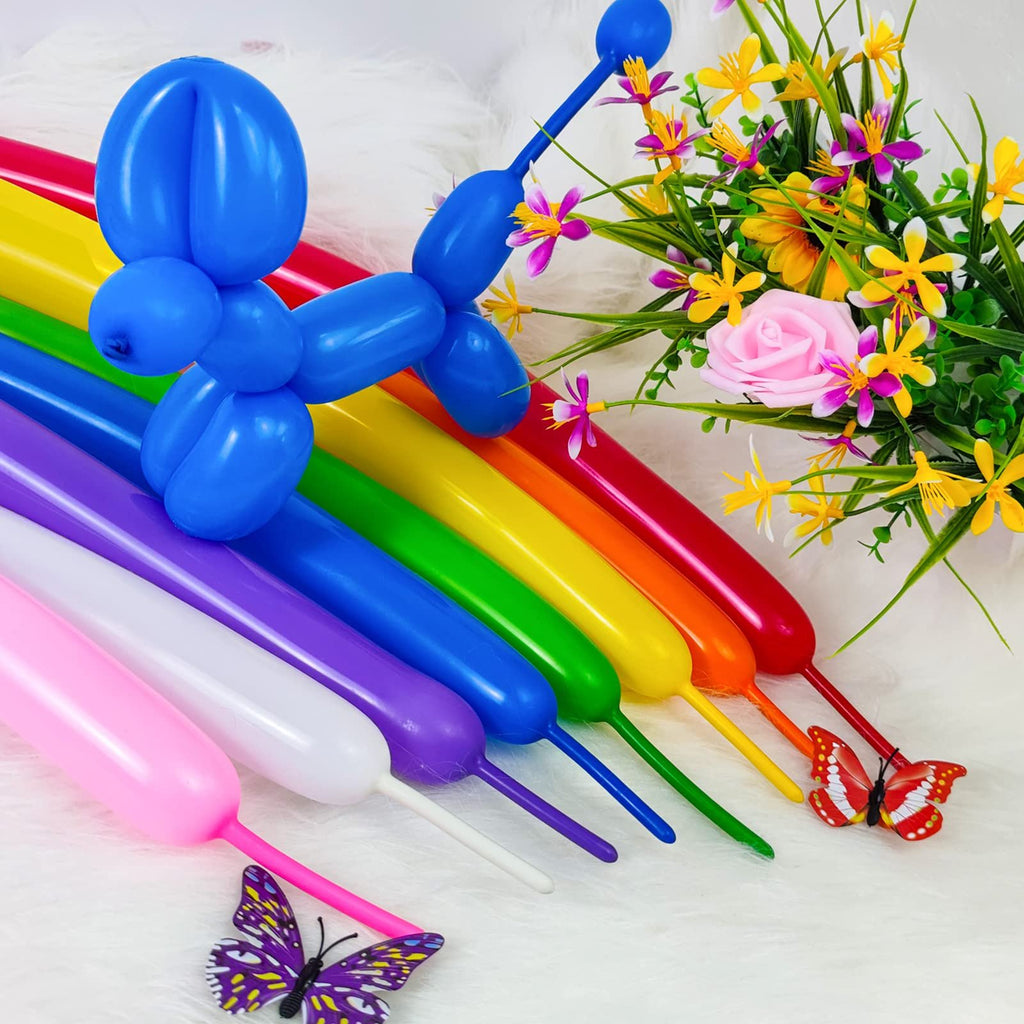 Assorted color twisting balloons arranged in a rainbow pattern with a blue balloon dog on top, next to a floral arrangement and decorative butterflies.