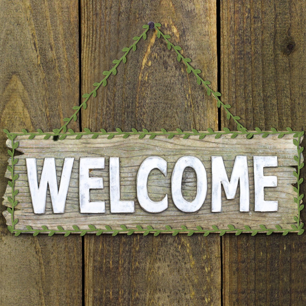 Wooden sign with WELCOME in silver letters, framed by green artificial leaf vine ribbon, hanging on a rustic wooden wall.