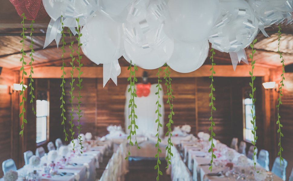 Artificial leaf vines hanging in front of a decorated event hall with tables and balloons