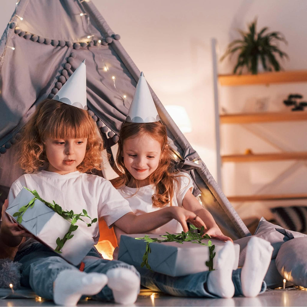 Two young girls in party hats opening gifts decorated with artificial leaf vines