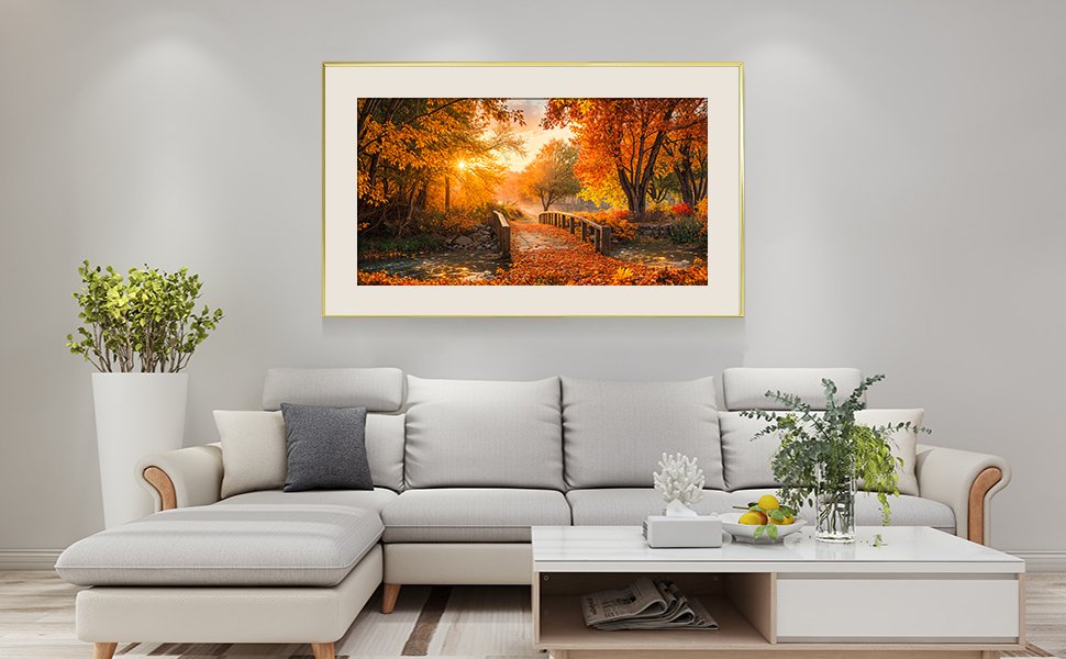 Framed diamond painting of a forest bridge in autumn, displayed above a sectional sofa.