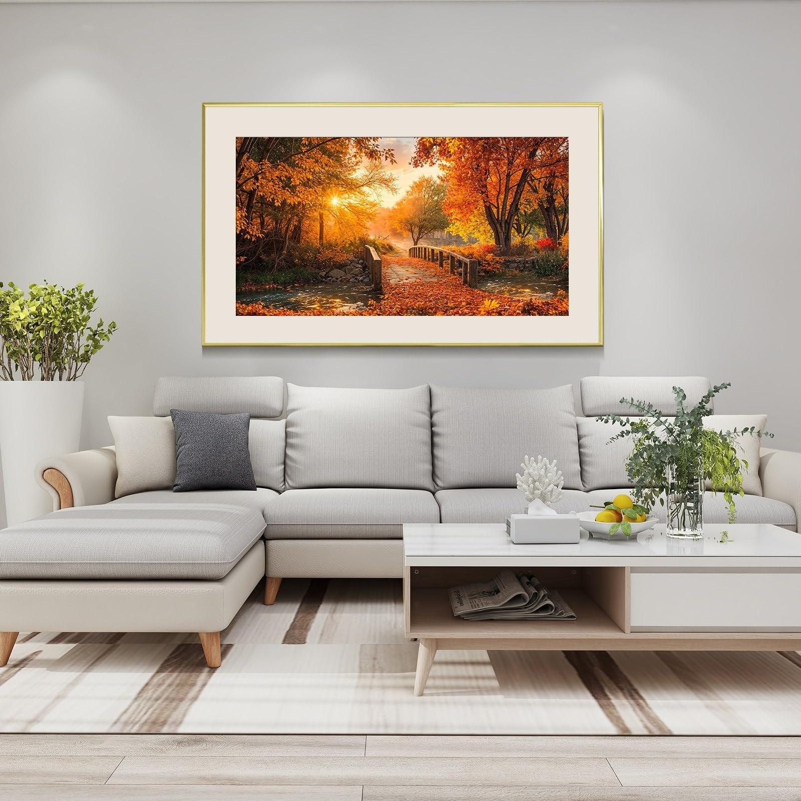 Framed diamond painting of a forest sunset with a bridge over a stream, displayed above a sofa.