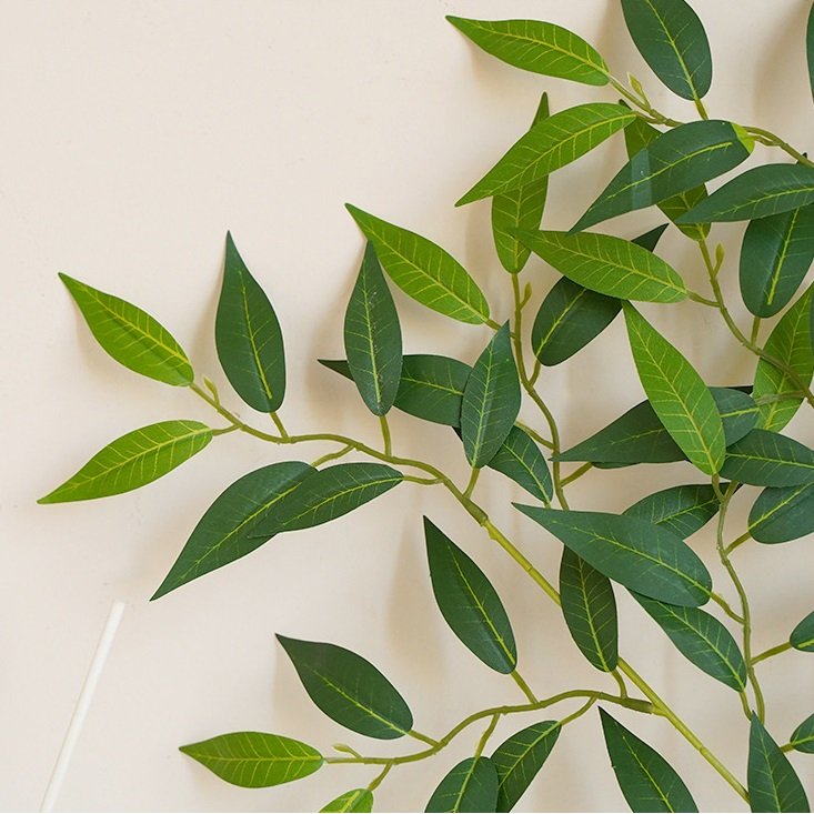 Close-up of artificial Italian Ruscus greenery stems with green leaves against a light background.