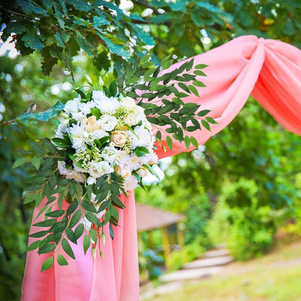 Artificial Italian Ruscus greenery stems draped on a pink fabric arch with a white floral arrangement.
