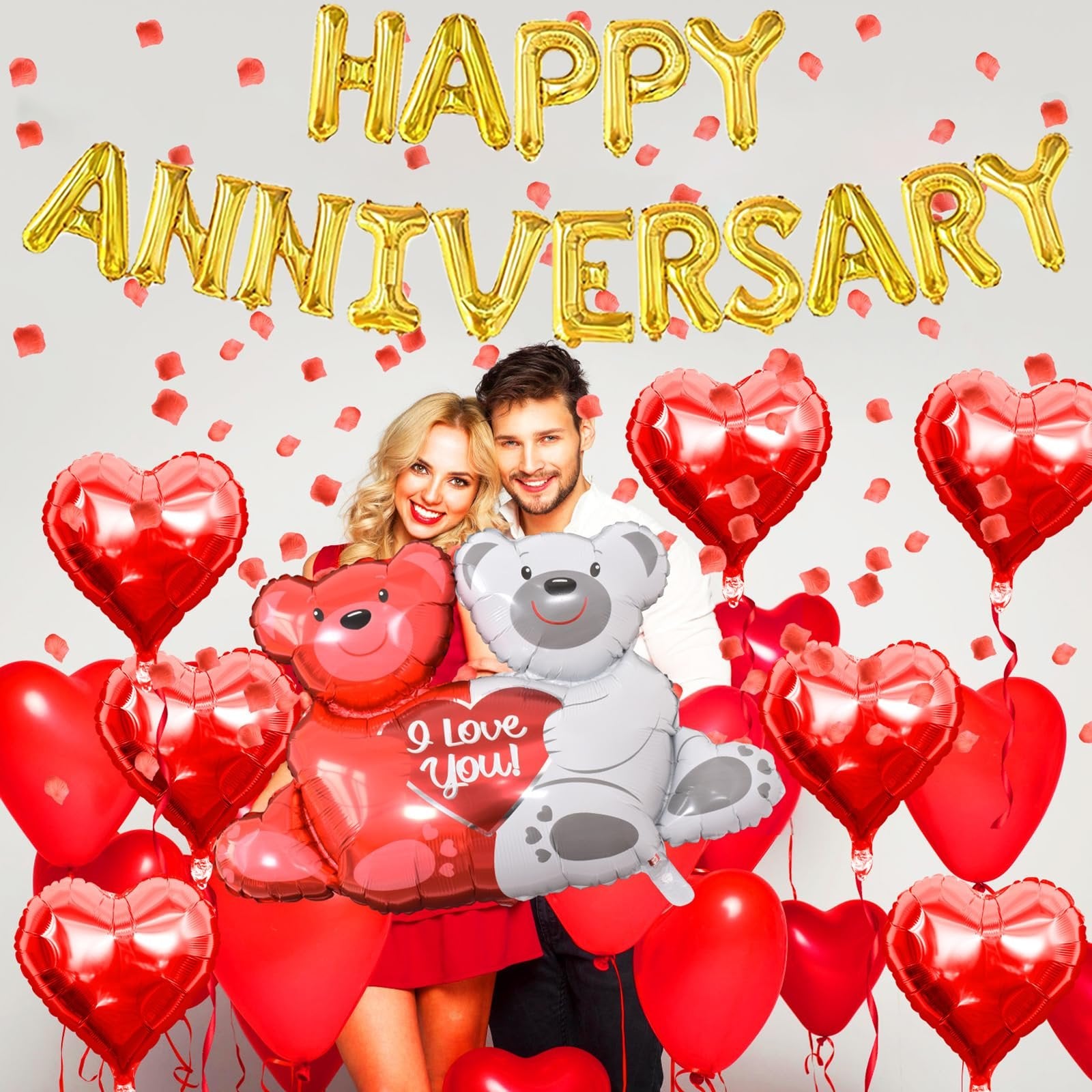 Couple posing with anniversary balloons including 'Happy Anniversary' banner, heart shapes, and teddy bears.