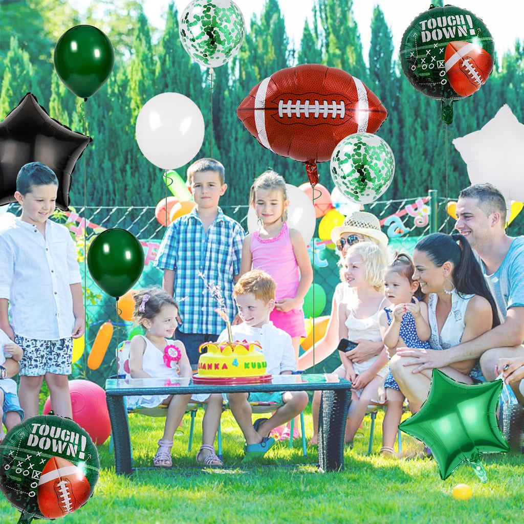 Family and children celebrating a birthday outdoors with football-themed balloons and a cake.