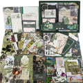 Scrapbooking kit contents including A6 grid notebook, stickers, papers, and vintage ephemera laid out flat.