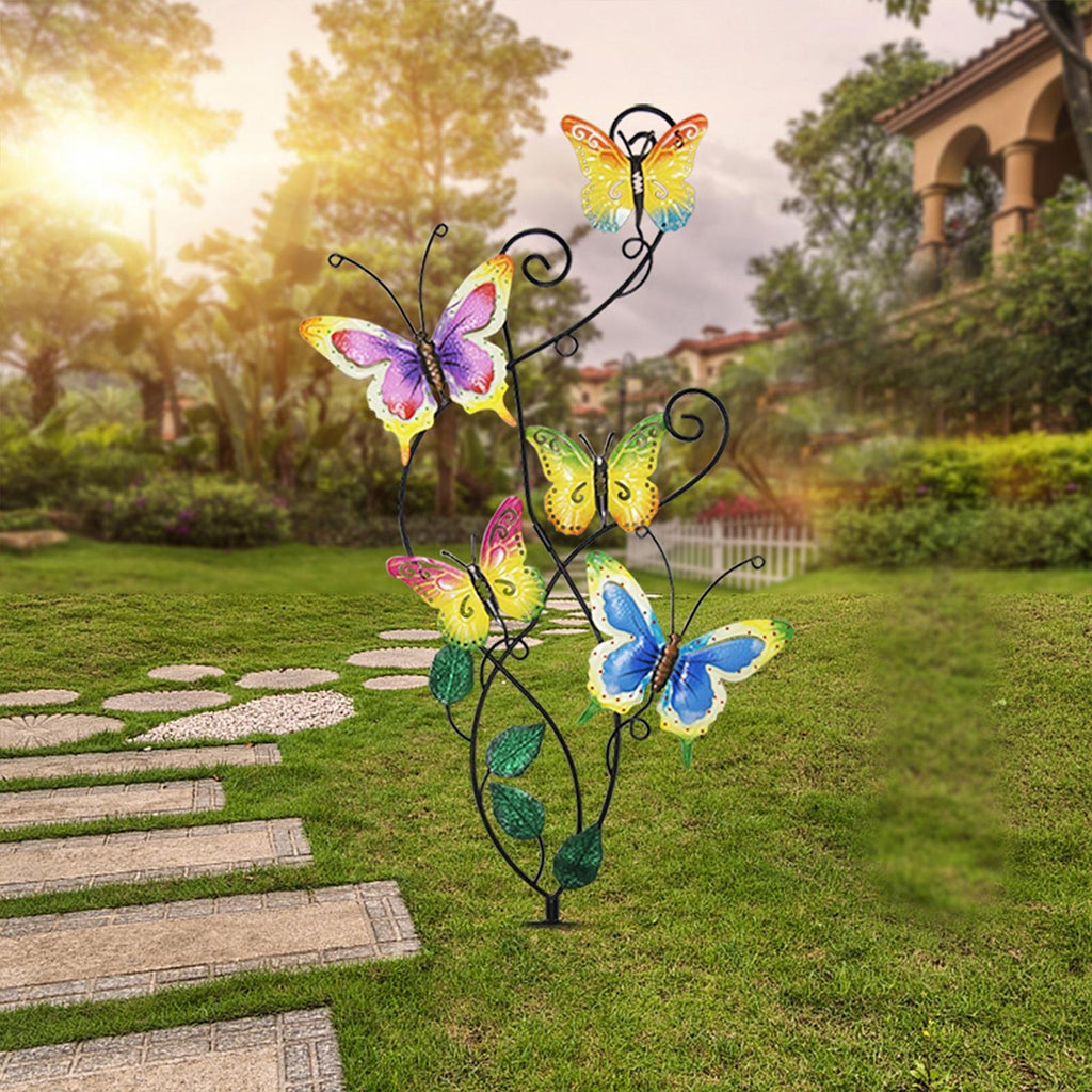 Metal garden stake with five colorful butterflies and green leaves, set in a grassy yard with a stone pathway.