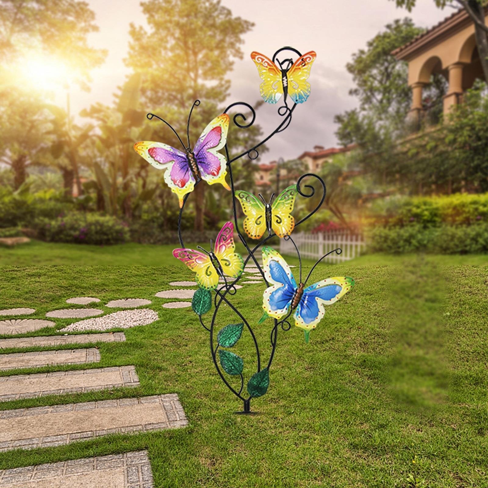 Metal garden stake with five colorful butterflies and green leaves, set in a grassy yard with a stone pathway.