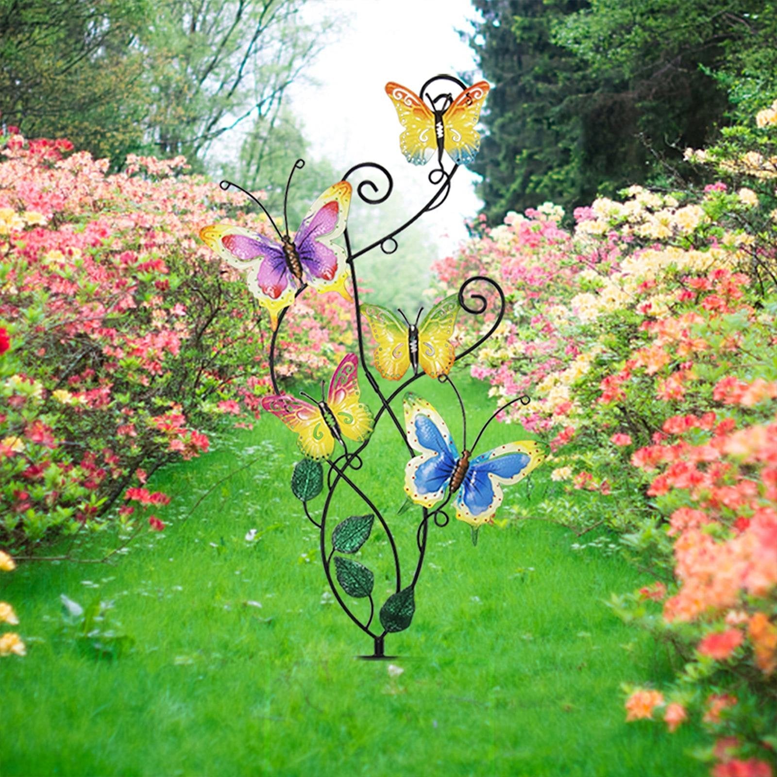 Metal garden stake with five colorful butterflies and green leaves, set in a garden with blooming bushes.