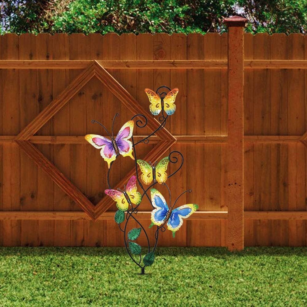 Metal garden stake with five colorful butterflies and green leaves, set against a wooden fence and grass.