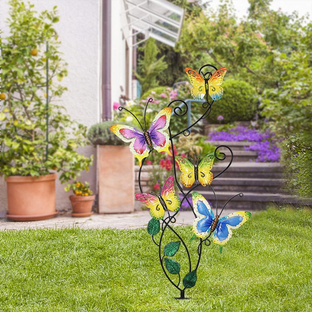 Metal garden stake with five colorful butterflies and green leaves, set in a garden with a house and stairs in the background.