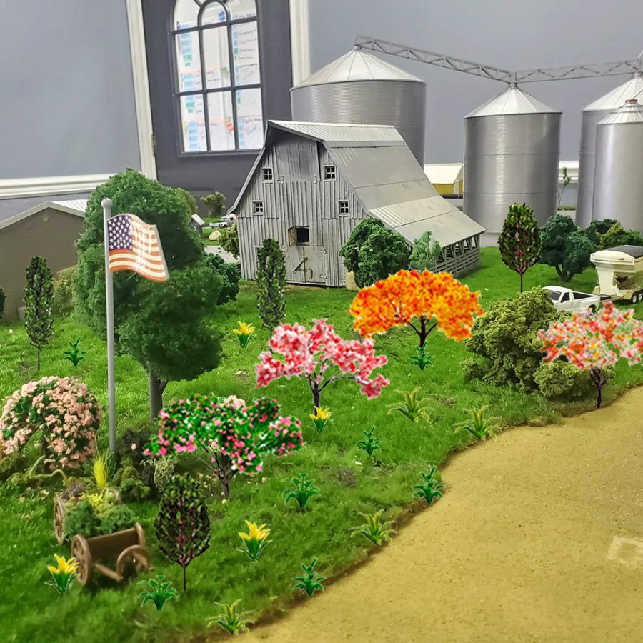 Miniature farm scene with barn, silos, trees, and American flag on a grassy landscape.