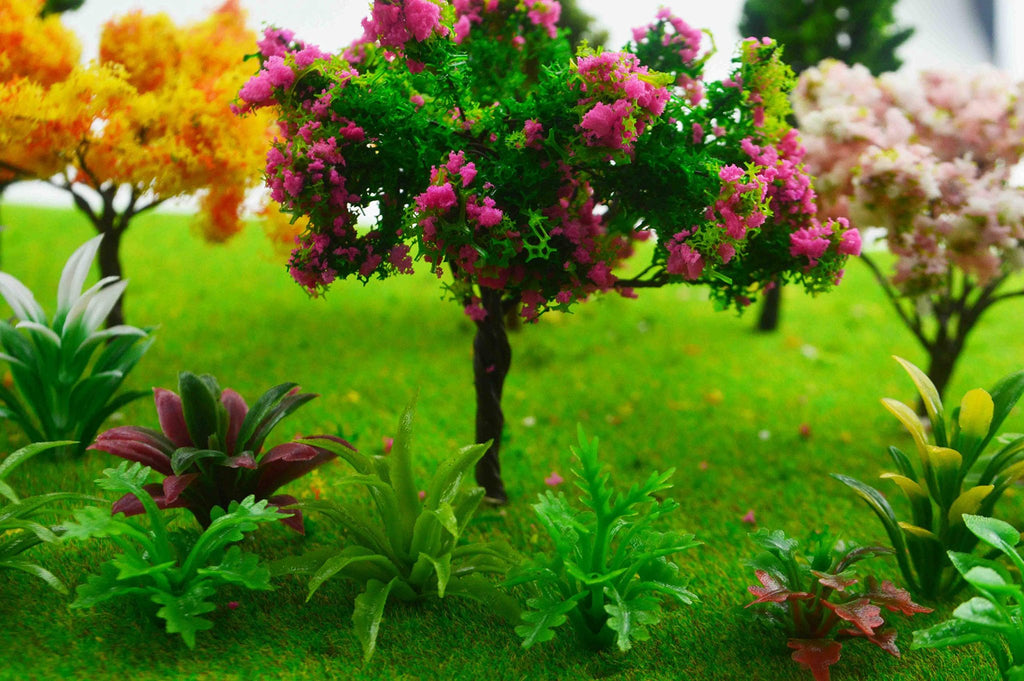 Assortment of miniature trees and plants with pink and yellow foliage on a green grassy landscape, close-up view.