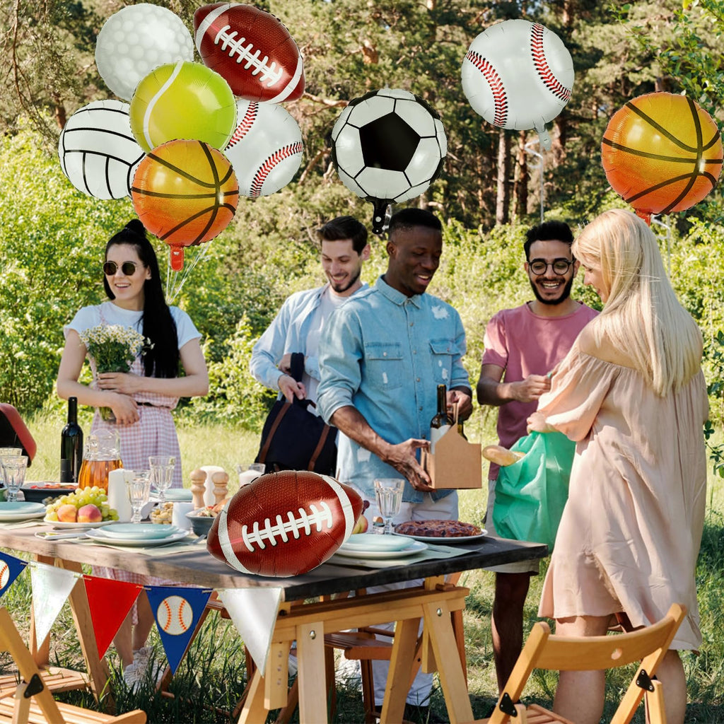 Group of people at an outdoor picnic table with sports-themed balloons including baseball, basketball, soccer, and football designs.