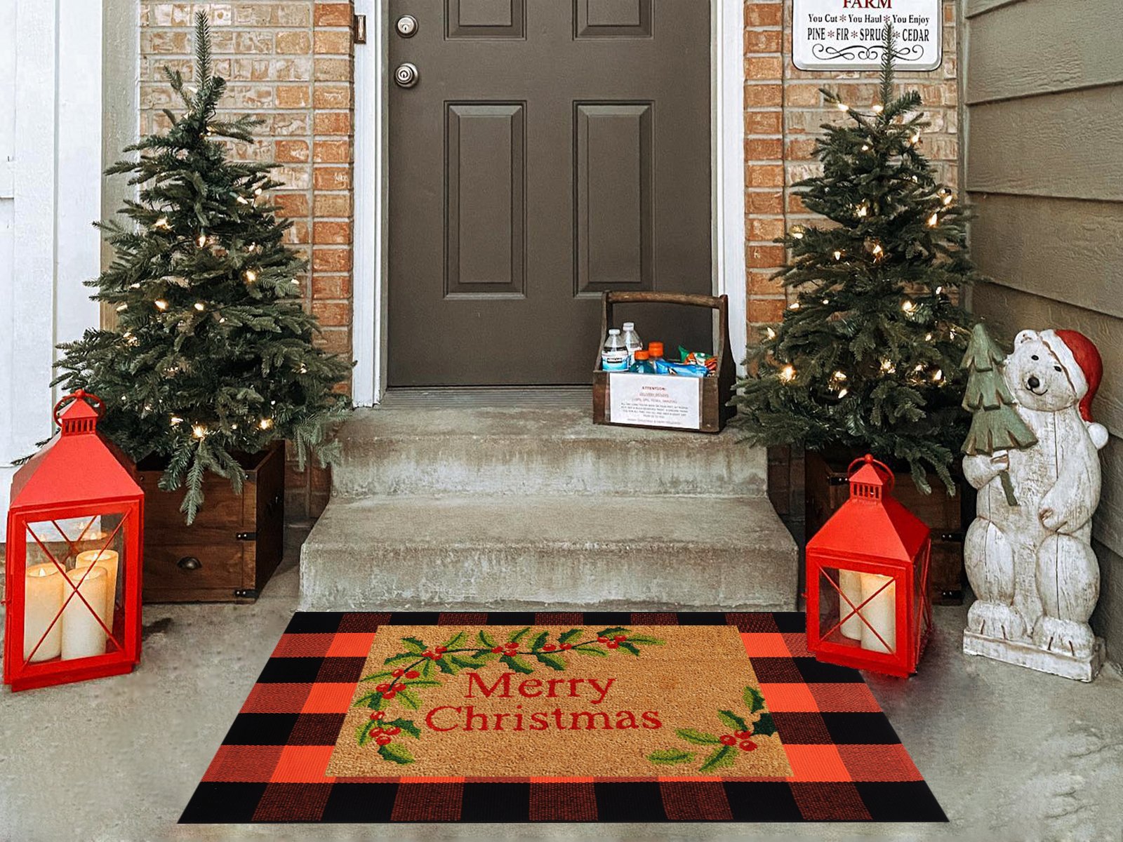 Buffalo plaid doormat with 'Merry Christmas' text and holly design, placed on a porch with Christmas trees and lanterns.