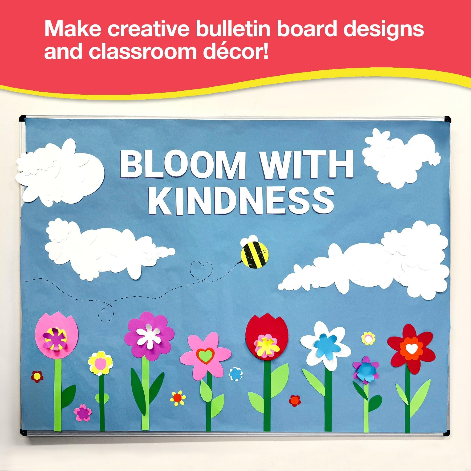 Bulletin board decorated with paper flowers, clouds, and a bee with the words 'Bloom With Kindness' displayed.