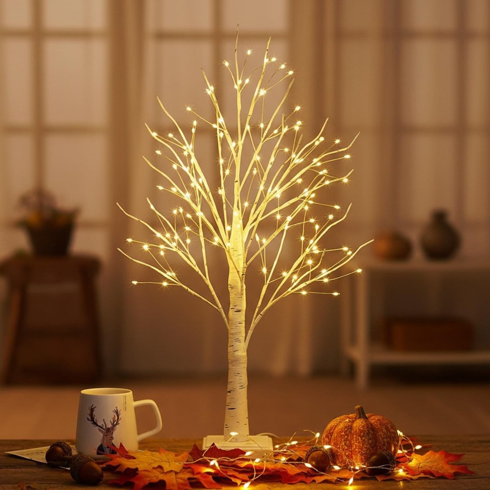 White birch tabletop tree with 144 warm white LED lights, set on a wooden table with autumn leaves, acorns, and a decorative pumpkin.
