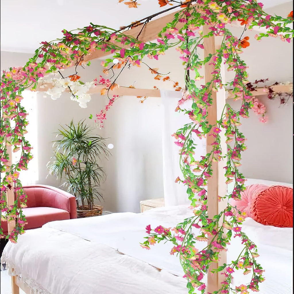 Artificial silk daisy vine garland with pink flowers and green leaves draped over a wooden canopy bed.