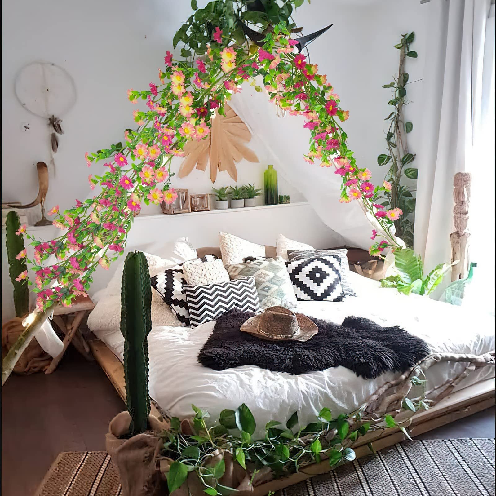 Artificial silk daisy vine garland with pink and yellow flowers draped over a bed with decorative pillows and a hat.