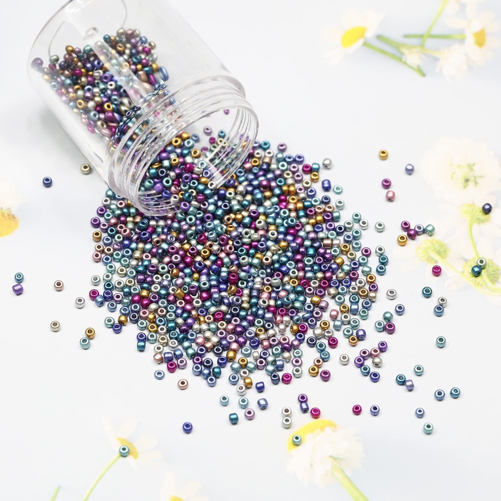 Assorted iridescent glass seed beads spilled from a clear container onto a light blue surface with blurred floral accents.