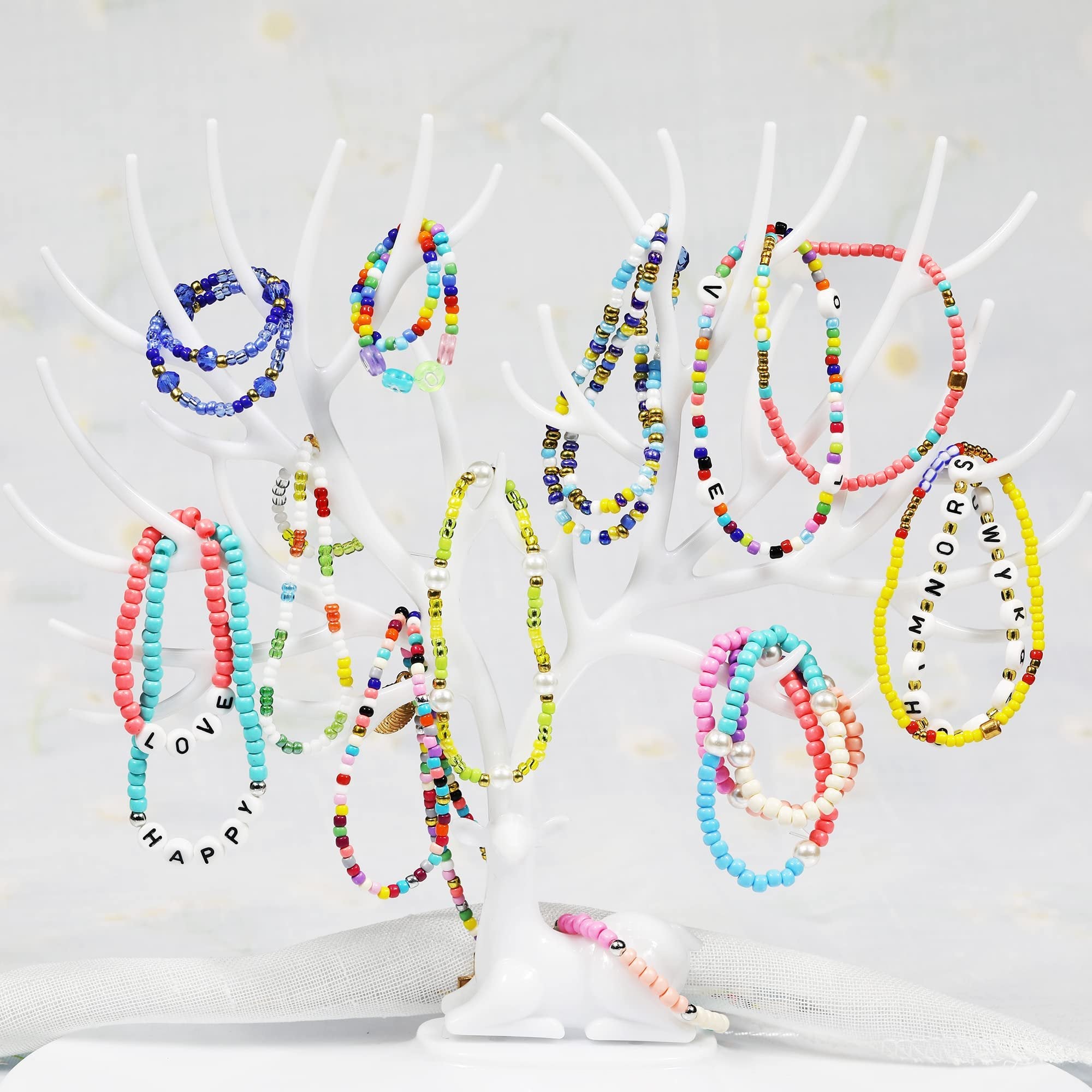 Assorted colorful beaded bracelets displayed on a white tree stand, some with letter beads spelling words.