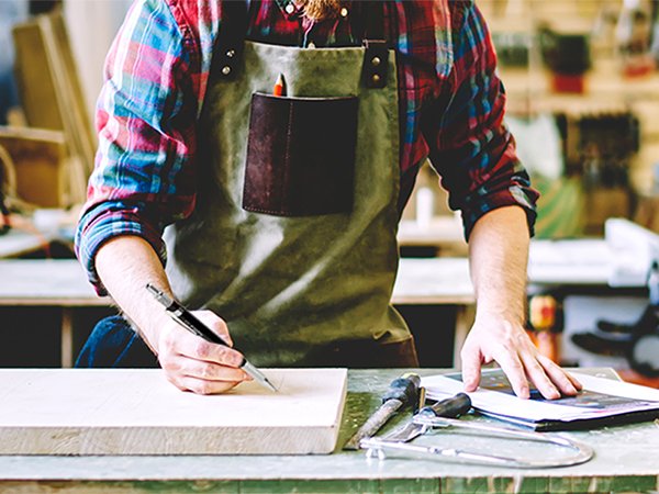 Person in plaid shirt and apron drawing on wood with a mechanical pencil