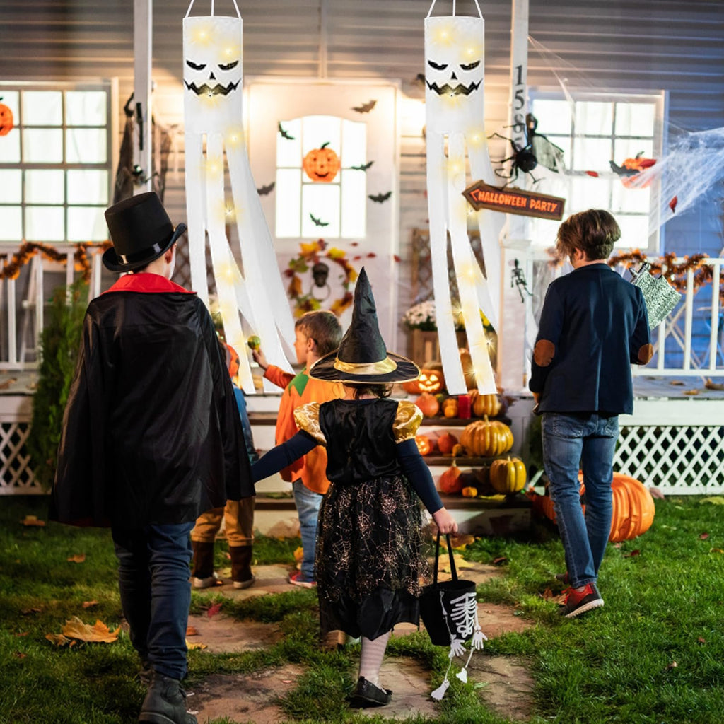 Children in Halloween costumes walk towards a decorated house with ghost windsocks hanging