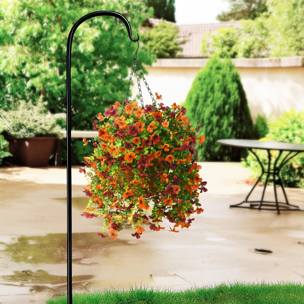 Hanging basket of orange and burgundy faux silk daisy flowers with eucalyptus leaves on a black shepherd's hook in a backyard setting.