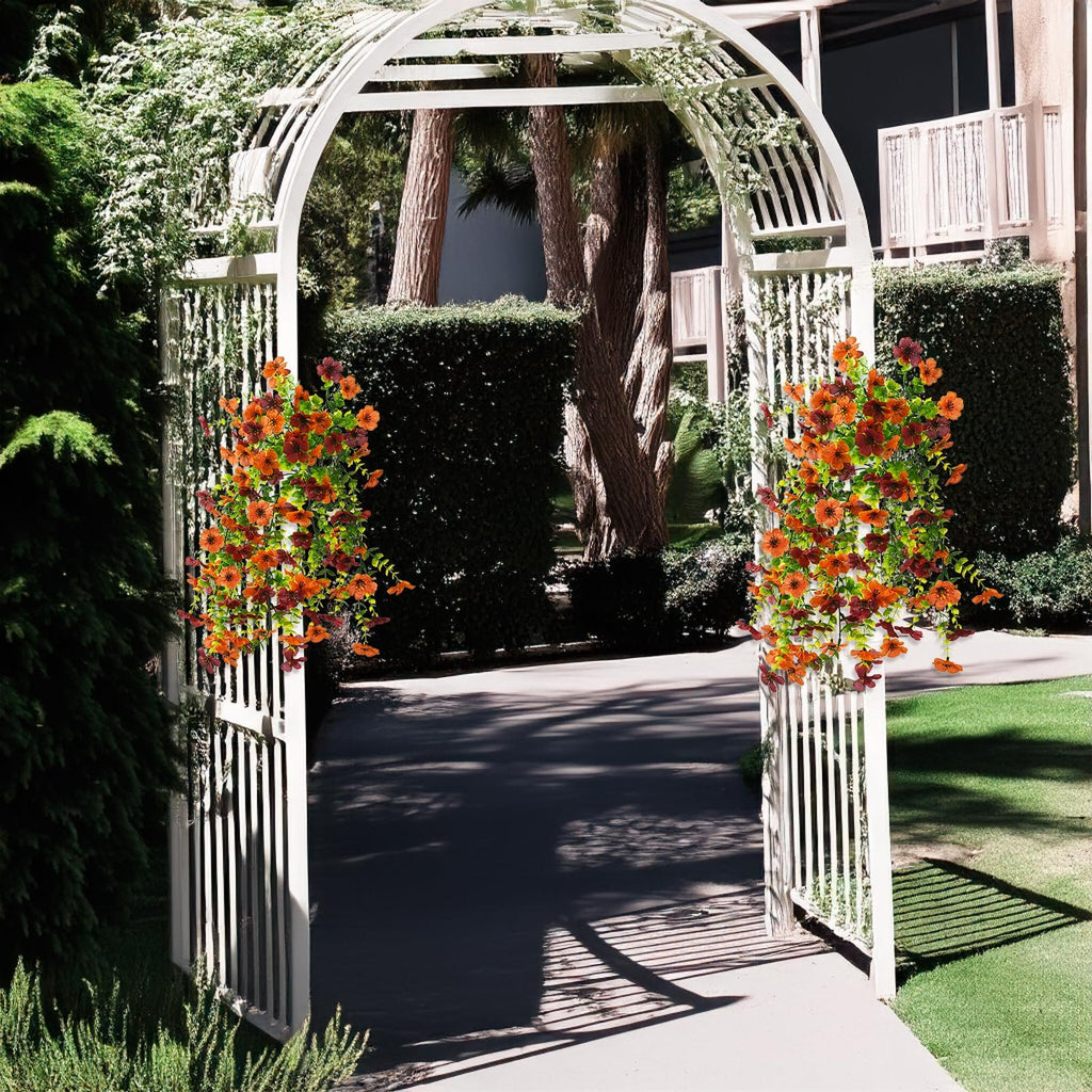 Two hanging arrangements of orange and brown faux silk daisy flowers with eucalyptus leaves adorn a white garden archway.