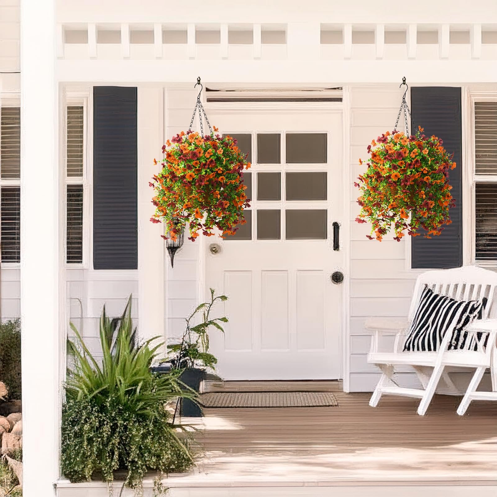 Two hanging baskets of orange and brown artificial flowers with eucalyptus leaves on a porch.
