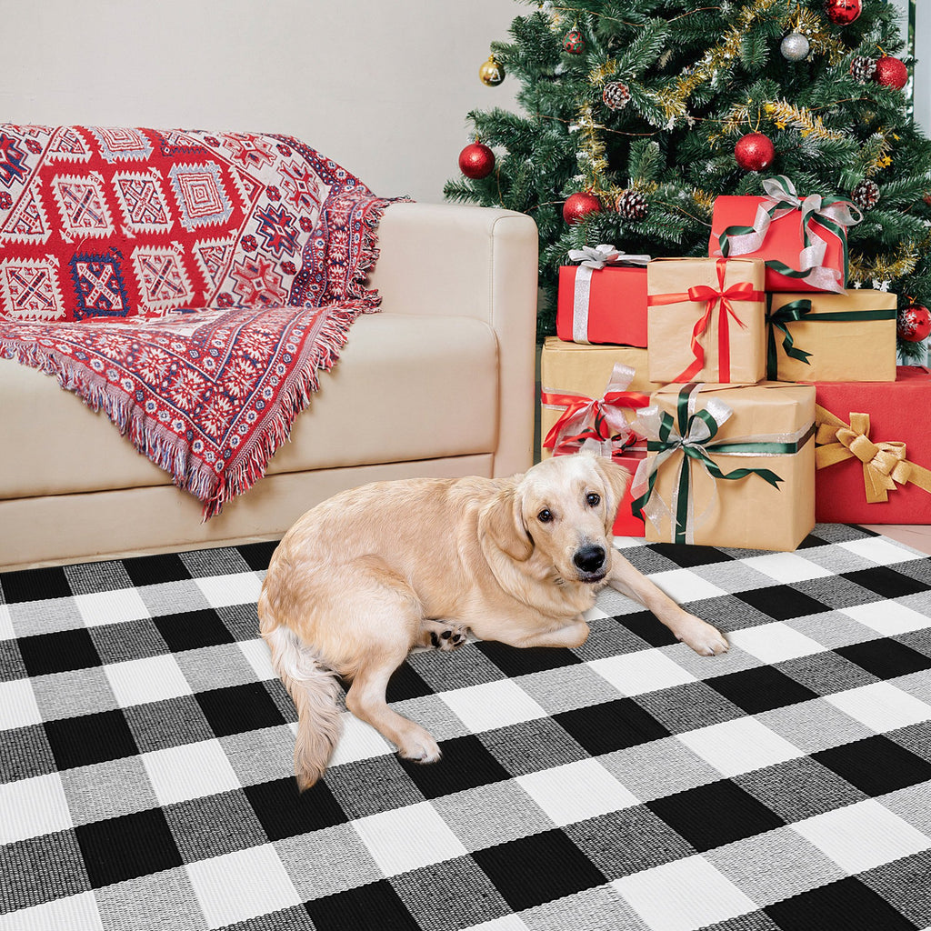 Golden retriever dog lying on a black and white buffalo plaid rug in front of a couch and Christmas tree with gifts