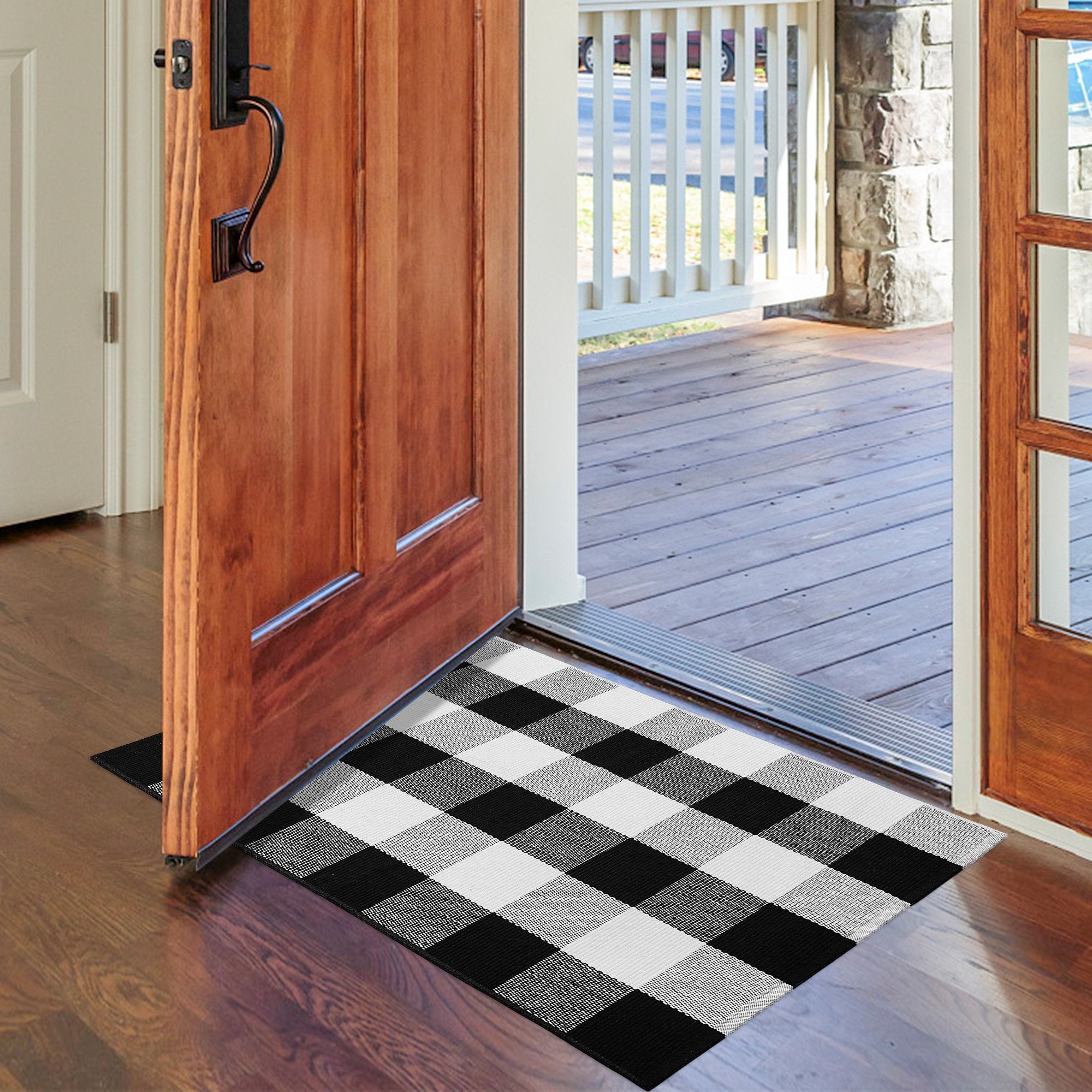 Buffalo plaid outdoor rug placed on a wooden floor inside an entryway, with a wooden door open to a porch.